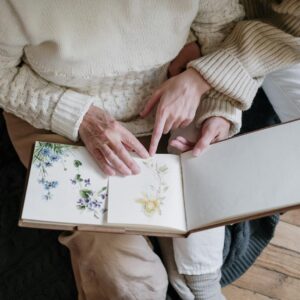 Two women reviewing a family photo album with floral artwork, creating memories together.