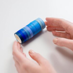 Close-up of hands arranging blue washi tape rolls on a white background, emphasizing creativity.